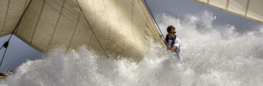 Classic yacht punching through spray with a crew member at the bow